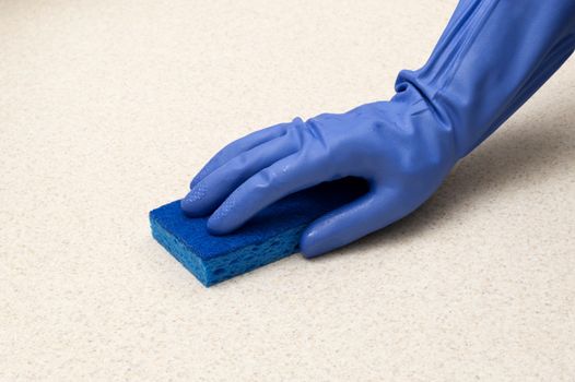 Close up shot of blue gloves and blue sponge cleaning counter top.