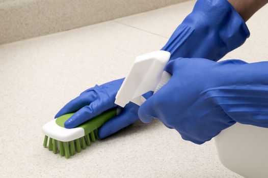 Hands wearing rubber gloves scrubbing counter with brush.