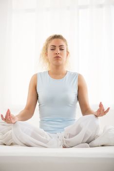 Cute young beautiful girl at morning doing yoga on the bed