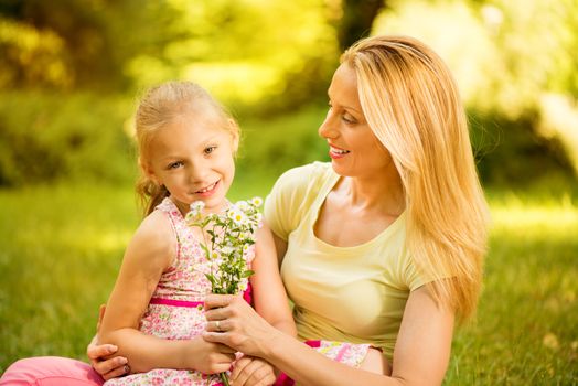 Cute little girl and her mother with bouquet flowers in the park