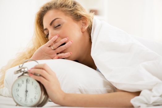 Young woman lying in bed in the morning. She is waking up with alarm clock.