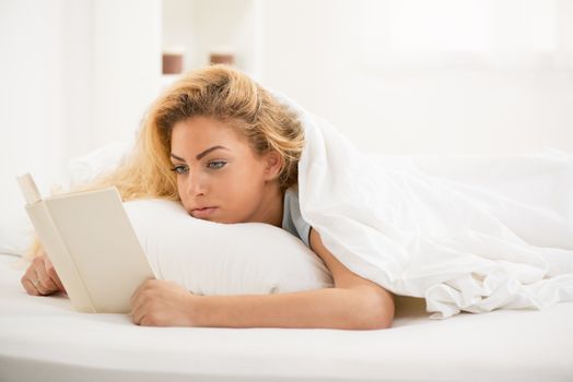 Cute young beautiful woman reading book in the bed