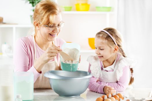 Beautiful happy grandmother learning her granddaughter Baking in a kitchen. 