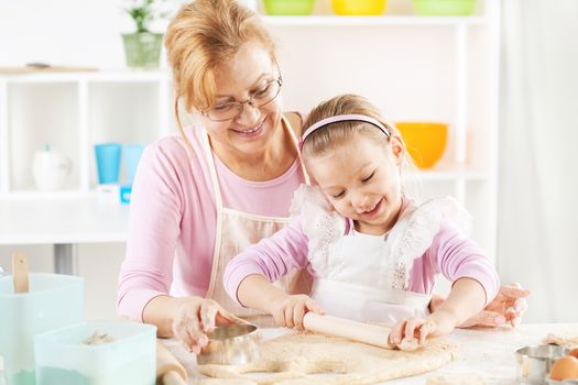 Beautiful happy grandmother and granddaughter a rolling pin together in the Kitchen. 