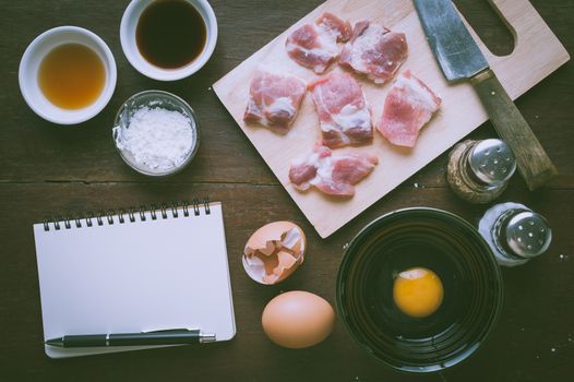 Preparation for cooking in home kitchen. Soft pork ribs on chopping board, notepad for check list, egg, and ingredients on wood table with vintage filter effect