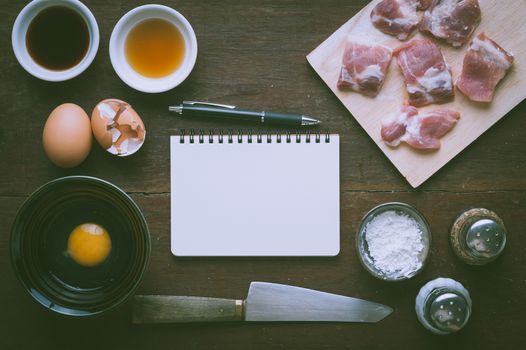 Preparation for cooking in home kitchen. Soft pork ribs on chopping board, notepad for check list, egg, and ingredients on wood table with vintage filter effect