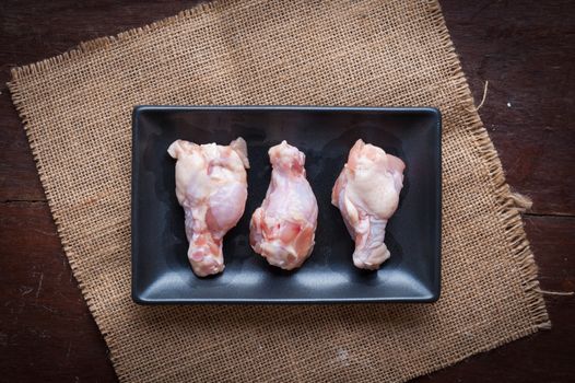 Preparation for cooking in home kitchen. Chicken wings in ceramic dish on wood table.