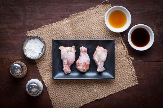 Preparation for cooking in home kitchen. Chicken wings in ceramic dish and ingredients on wood table.