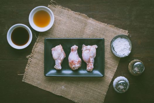 Preparation for cooking in home kitchen. Chicken wings in ceramic dish and ingredients on wood table with vintage filter effect.