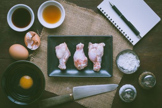Preparation for cooking in home kitchen. Chicken wings in ceramic dish and ingredients on wood table with vintage filter effect.