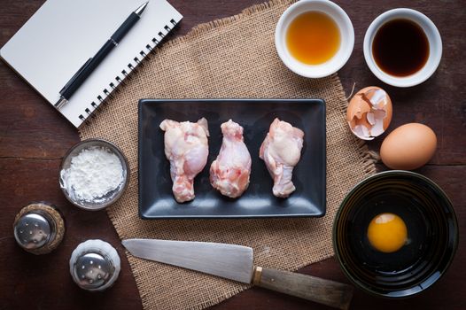 Preparation for cooking in home kitchen. Chicken wings in ceramic dish and ingredients on wood table.