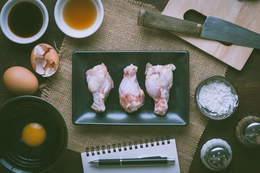 Preparation for cooking in home kitchen. Chicken wings in ceramic dish and ingredients on wood table with vintage filter effect.