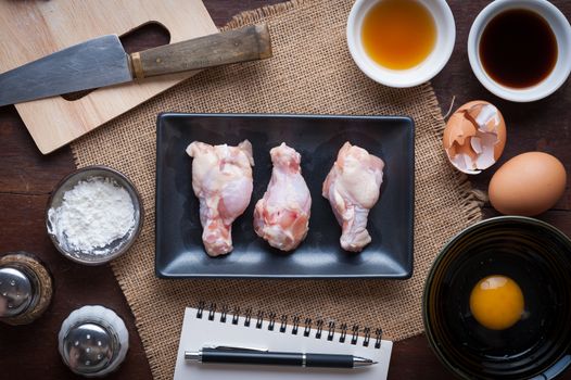 Preparation for cooking in home kitchen. Chicken wings in ceramic dish and ingredients on wood table.