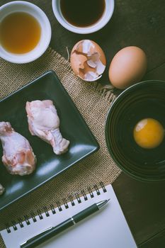 Preparation for cooking in home kitchen. Chicken wings in ceramic dish and ingredients on wood table with vintage filter effect.