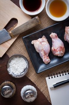 Preparation for cooking in home kitchen. Chicken wings in ceramic dish and ingredients on wood table.