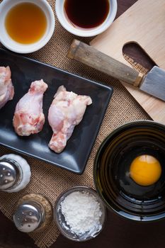 Preparation for cooking in home kitchen. chicken wings in ceramic dish, eggs, and ingredients on wood table.
