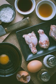 Preparation for cooking in home kitchen. chicken wings in ceramic dish, eggs, and ingredients on wood table with vintage filter effect.