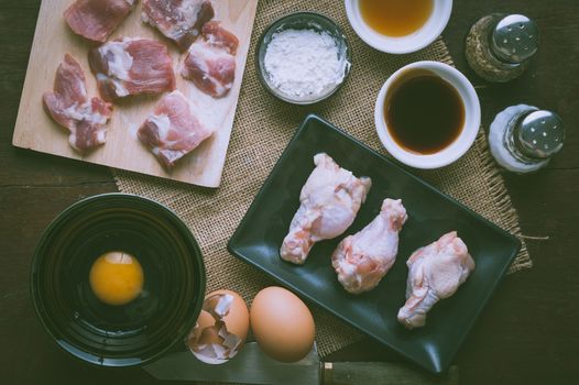 Preparation for cooking in home kitchen. Soft pork ribs on chopping board, chicken wings in ceramic dish, eggs, and ingredients on wood table with vintage filter effect.