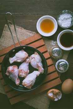 Preparation for cooking in home kitchen. chicken wings in small pan, eggs, and ingredients on wood table with vintage filter effect