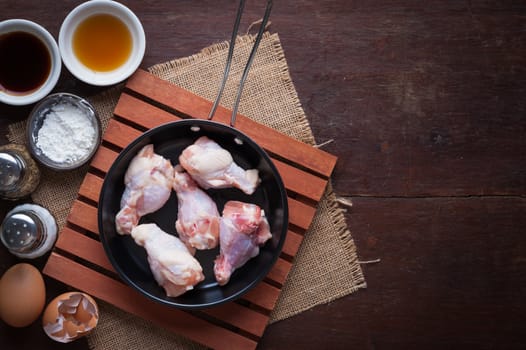 Preparation for cooking in home kitchen. chicken wings in small pan, eggs, and ingredients on wood table with low key scene