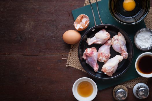Preparation for cooking in home kitchen. chicken wings in small pan, eggs, and ingredients on wood table with blank area for text or message.