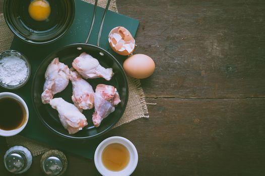 Preparation for cooking in home kitchen. chicken wings in small pan, eggs, and ingredients on wood table with blank area for text or message with vintage filter effect.