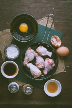 Preparation for cooking in home kitchen. chicken wings in small pan, eggs, and ingredients on wood table with vintage filter effect