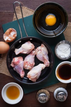 Preparation for cooking in home kitchen. chicken wings in small pan, eggs, and ingredients on wood table.