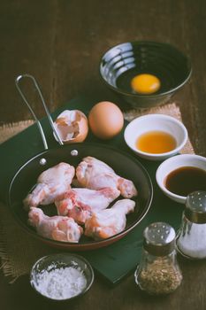 Preparation for cooking in home kitchen. chicken wings in small pan, eggs, and ingredients on wood table with vintage filter effect