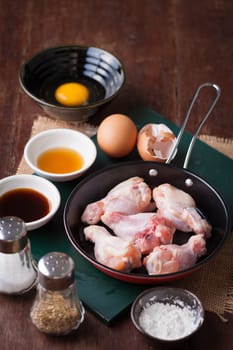Preparation for cooking in home kitchen. chicken wings in small pan, eggs, and ingredients on wood table.