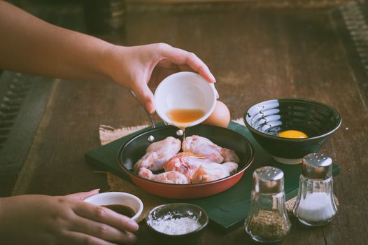 Preparation for cooking in home kitchen. woman left hand pouring soil sauce into fry pan to mix with chicken wings