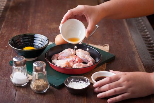 Preparation for cooking in home kitchen. woman right hand pouring soil sauce into fry pan to mix with chicken wings