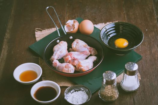 Preparation for cooking in home kitchen. chicken wings in small pan, eggs, and ingredients on wood table with vintage filter effect