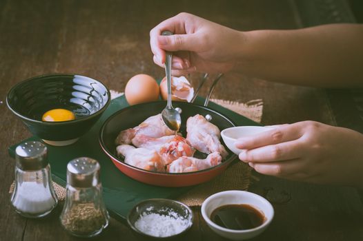 Preparation for cooking in home kitchen. Woman right hand pouring oyster sauce into fry pan to mix with chicken wings with vintage filter effect.