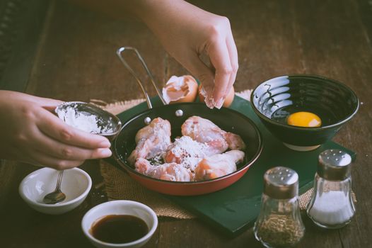 Preparation for cooking in home kitchen. Woman keft hand put corn flour into fry pan to mix with chicken wings with vintage filter effect.