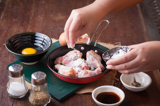 Preparation for cooking in home kitchen. Woman right hand put corn flour into fry pan to mix with chicken wings