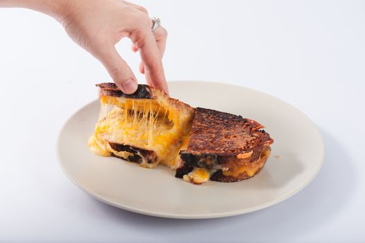 Toasted sandwich with various types of  cheese in ceramic dish. Woman hand try to open shell to show cheese inside.