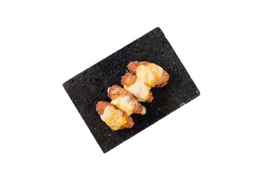 Deep fried chicken wings dressed with various types of cheese on black stone plate isolated on white background with clipping path