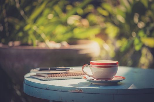 Coffee cup, notebooks, and pen on blue veteran table in morning time with vintage filter effect