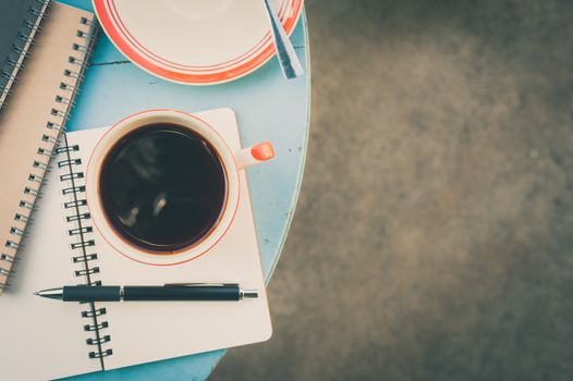 Top view of coffee cup with notebooks and pen on blue round wood table with vintage filter effect