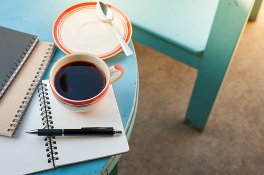 Coffee cup with notebooks and pen on blue round wood table in morning time