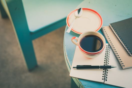 Coffee cup with notebooks and pen on blue round wood table in morning time with vintage filter effect