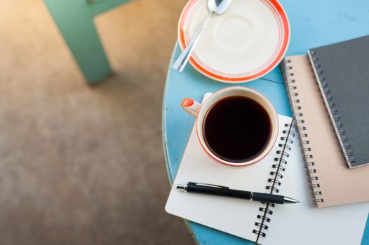 Coffee cup with notebooks and pen on blue round wood table in morning time