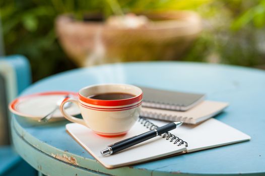 Coffee cup with notebooks and pen on blue round wood table in morning time