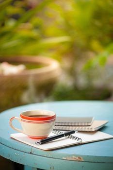 Coffee cup with notebooks and pen on blue round wood table in morning time