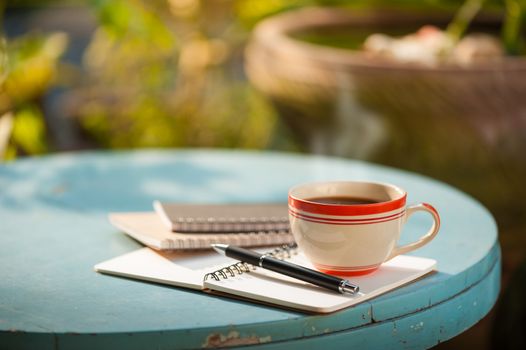 Coffee cup with notebooks and pen on blue round wood table in morning time
