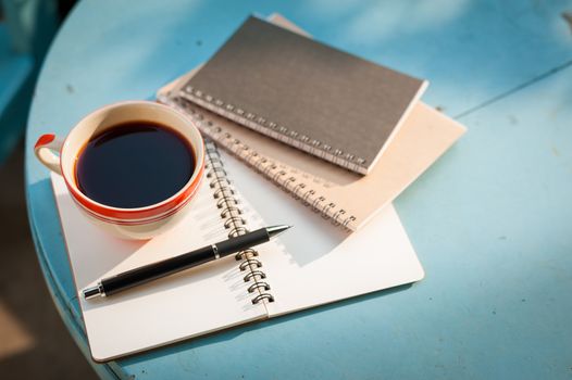 Coffee cup with notebooks and pen on blue round wood table in morning time