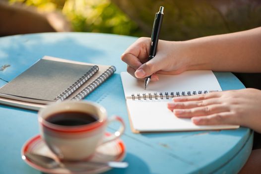 Woman right hand writing journal on small notebook at outdoor area in cafe with morning scene