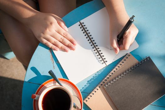 Woman left writing journal on small notebook in outdoor area at cafe with morning scene