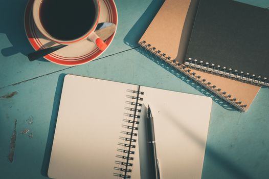 Morning scene of small notebook and pen beside coffee cup on blue wood table at outdoor area in cafe with vintage filter effect